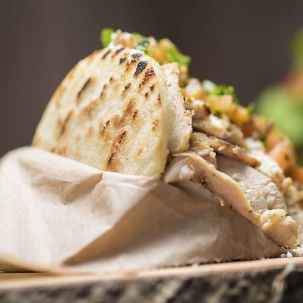 Close-up of a Venezuelan arepa filled with chicken and vegetables, served in brown paper.