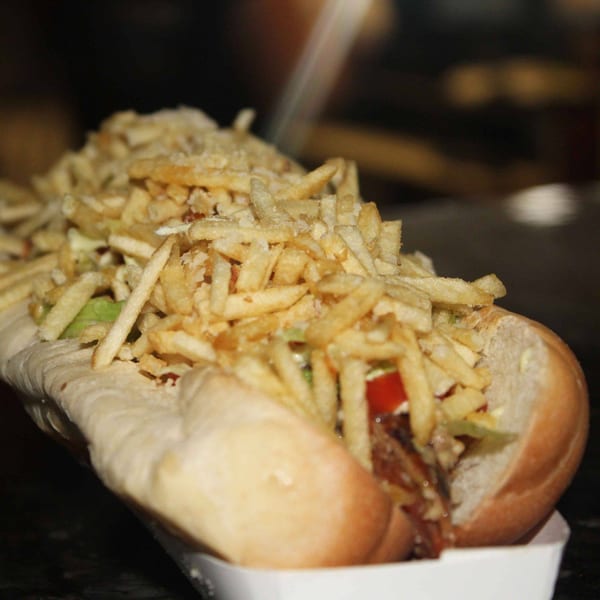 Close-up of a Venezuelan hot dog, loaded with crispy shoestring fries, tomatoes, and green sauce.