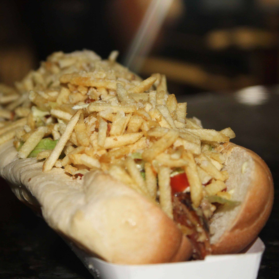Close-up of a Venezuelan hot dog, loaded with crispy shoestring fries, tomatoes, and green sauce.