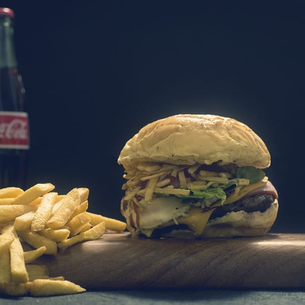 A Venezuelan burger with fries and a Coca-Cola bottle on a wooden board.