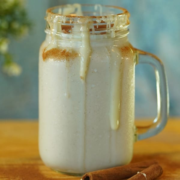 Venezuelan Chicha drink in a mason jar, garnished with cinnamon powder and two cinnamon sticks.
