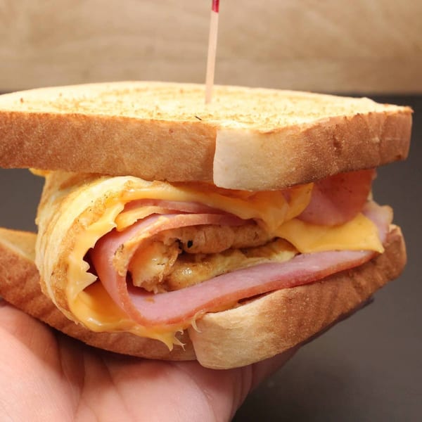 A hand holds a toasted sandwich filled with ham, cheese, and a fried egg.