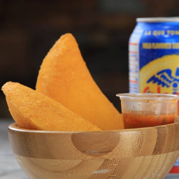 Two golden-fried Venezuelan empanadas in a wooden bowl with sauce and a soda can.