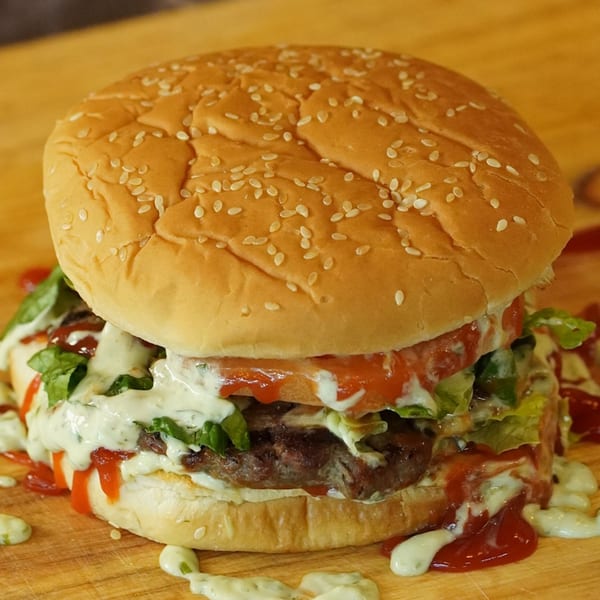 A large, juicy Venezuelan burger with lettuce, tomato, and generous amounts of white and red sauces.