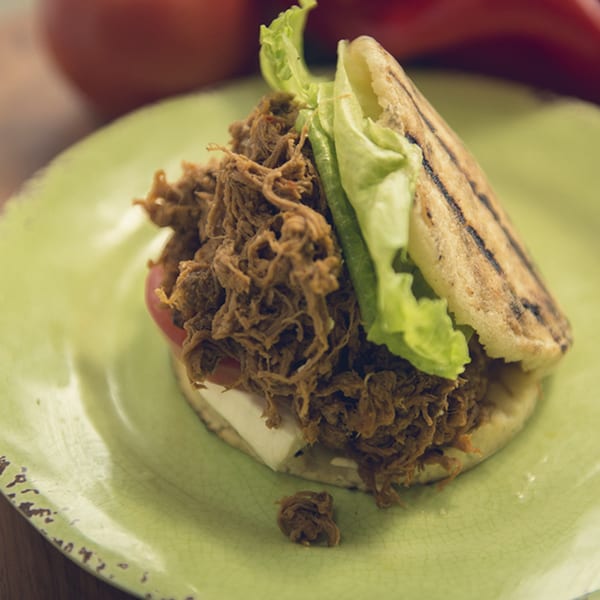A Venezuelan Eparepa arepa, filled with shredded beef, lettuce, tomato, and white cheese, on a green plate.