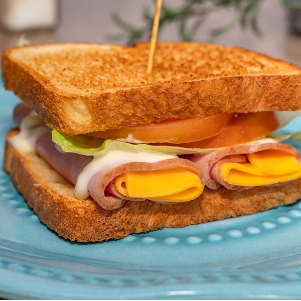 Toasted sandwich with ham, cheese, lettuce, tomato, and mayonnaise on a blue plate.